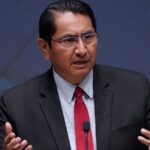 Jonathan Nez wearing a suit and red tie speaking at a podium