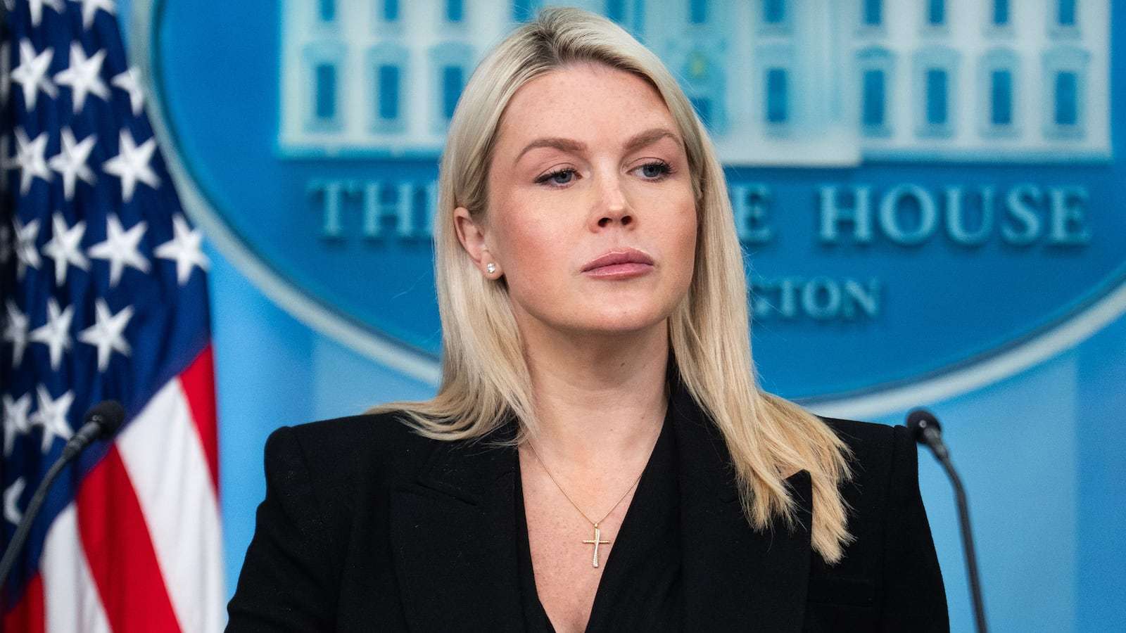 Former White House press secretary Karoline Leavitt standing at a podium with an American flag and W