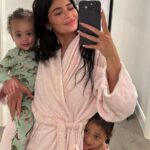 Kylie Jenner wearing a pink robe holding her young child indoors at home
