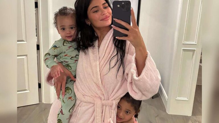 Kylie Jenner wearing a pink robe holding her young child indoors at home