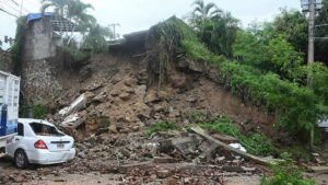 A white car damaged by a large landslide and debris after a storm