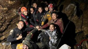 Group of rescued miners and rescue workers smiling inside a rocky cave in Laos