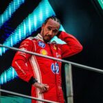 Lewis Hamilton wearing a red Ferrari racing suit with hand behind head