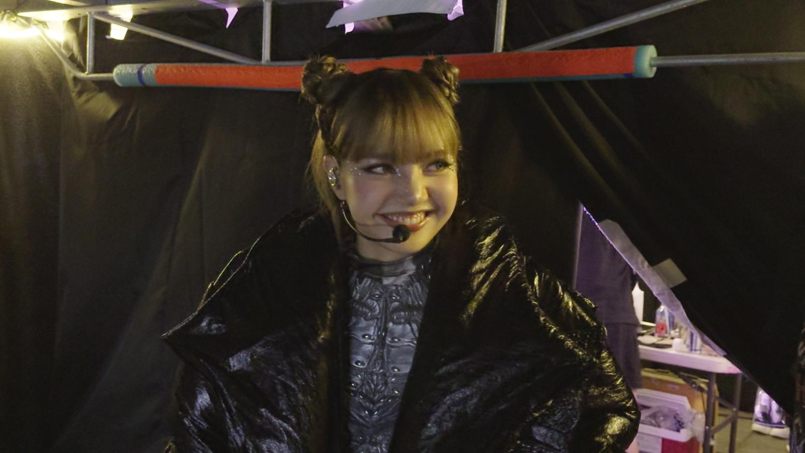 Lisa smiling while wearing a performance outfit and headset microphone backstage at a concert