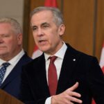 Prime Minister Mark Carney speaking at a podium with Canadian flags in the background
