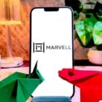 A smartphone displaying the Marvell logo sits on a desk with financial decorations