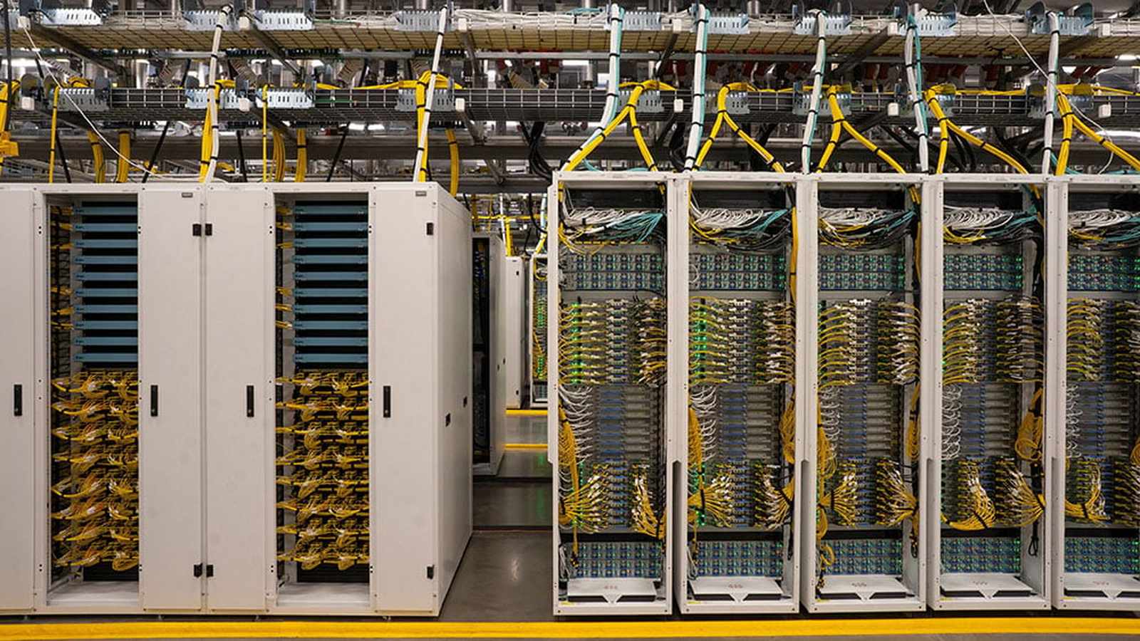 Rows of enterprise data center server racks with organized yellow network cables and overhead trays