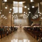 Wide view of a crowded modern Catholic cathedral interior during a service with parishioners seated