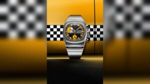 A close-up studio shot of a luxury stainless steel chronograph watch with a yellow and black dial ag