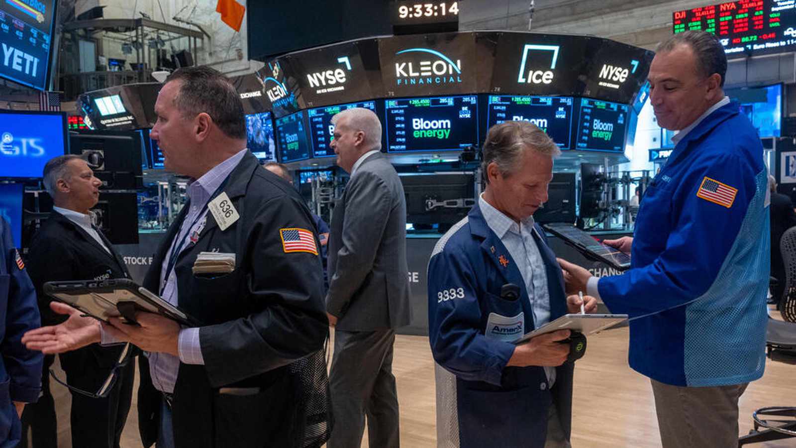 Traders working on the New York Stock Exchange floor with digital ticker boards in the background