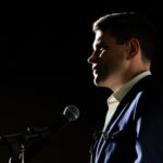 Profile view of a man in a suit speaking into a microphone