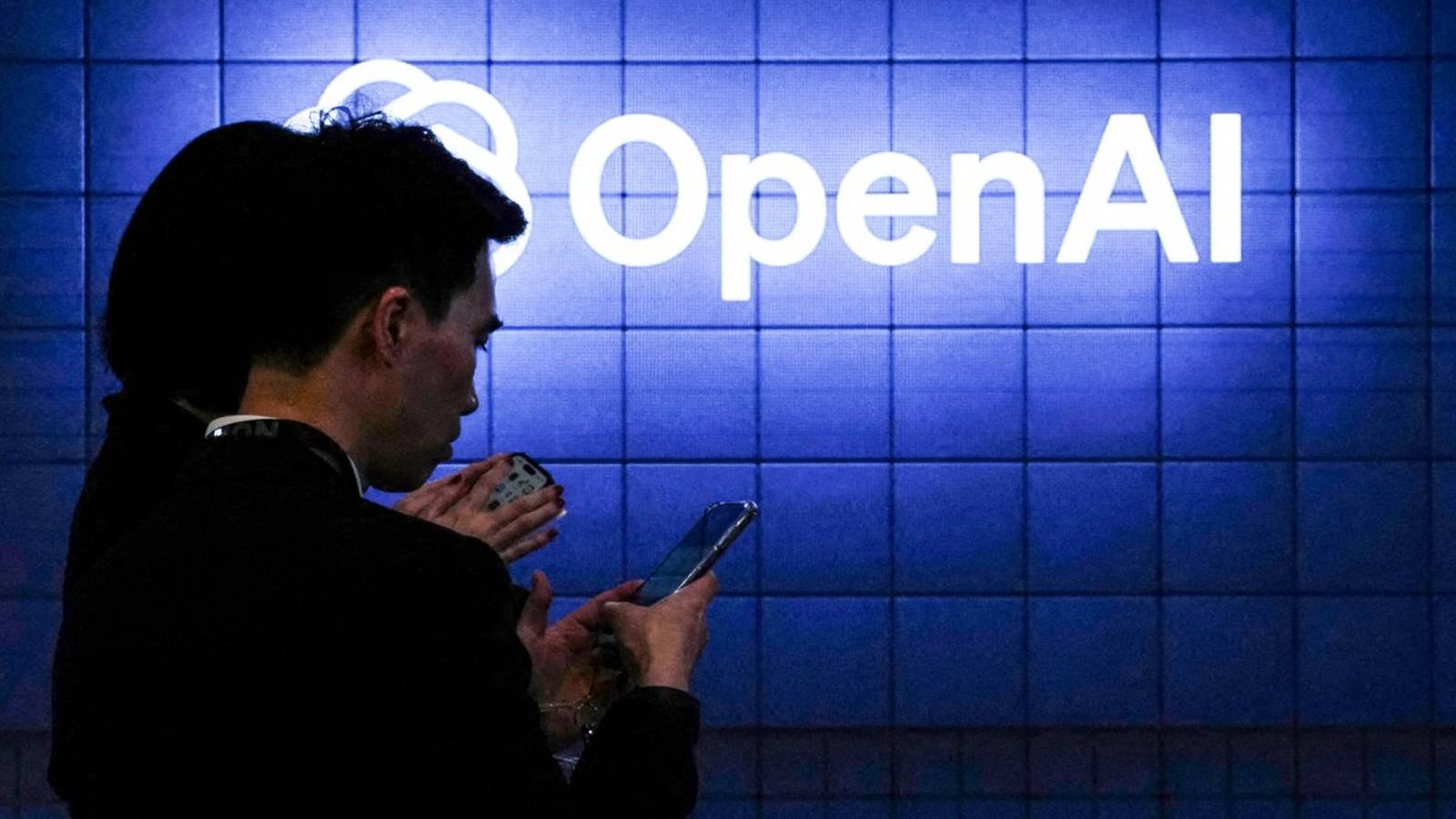 Silhouettes of people looking at smartphones in front of a blue tiled wall with the illuminated whit