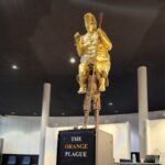 A 2.5-metre golden statue titled The Orange Plague displayed indoors inside a parliamentary building