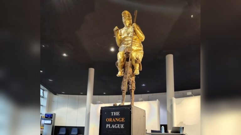 A 2.5-metre golden statue titled The Orange Plague displayed indoors inside a parliamentary building