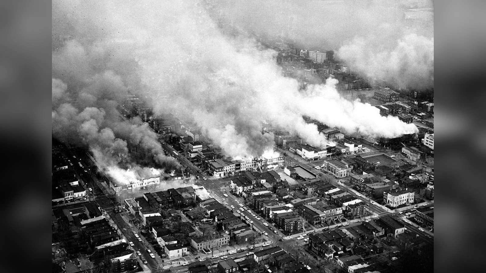 Military jeep driving past burning building during 1968 Washington D.C. riots after MLK assassinatio