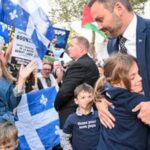 Politician Paul St-Pierre Plamondon hugging a child amidst supporters waving Quebec flags during an