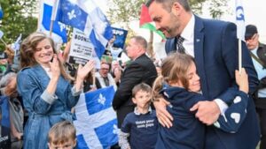 Politician Paul St-Pierre Plamondon hugging a child amidst supporters waving Quebec flags during an