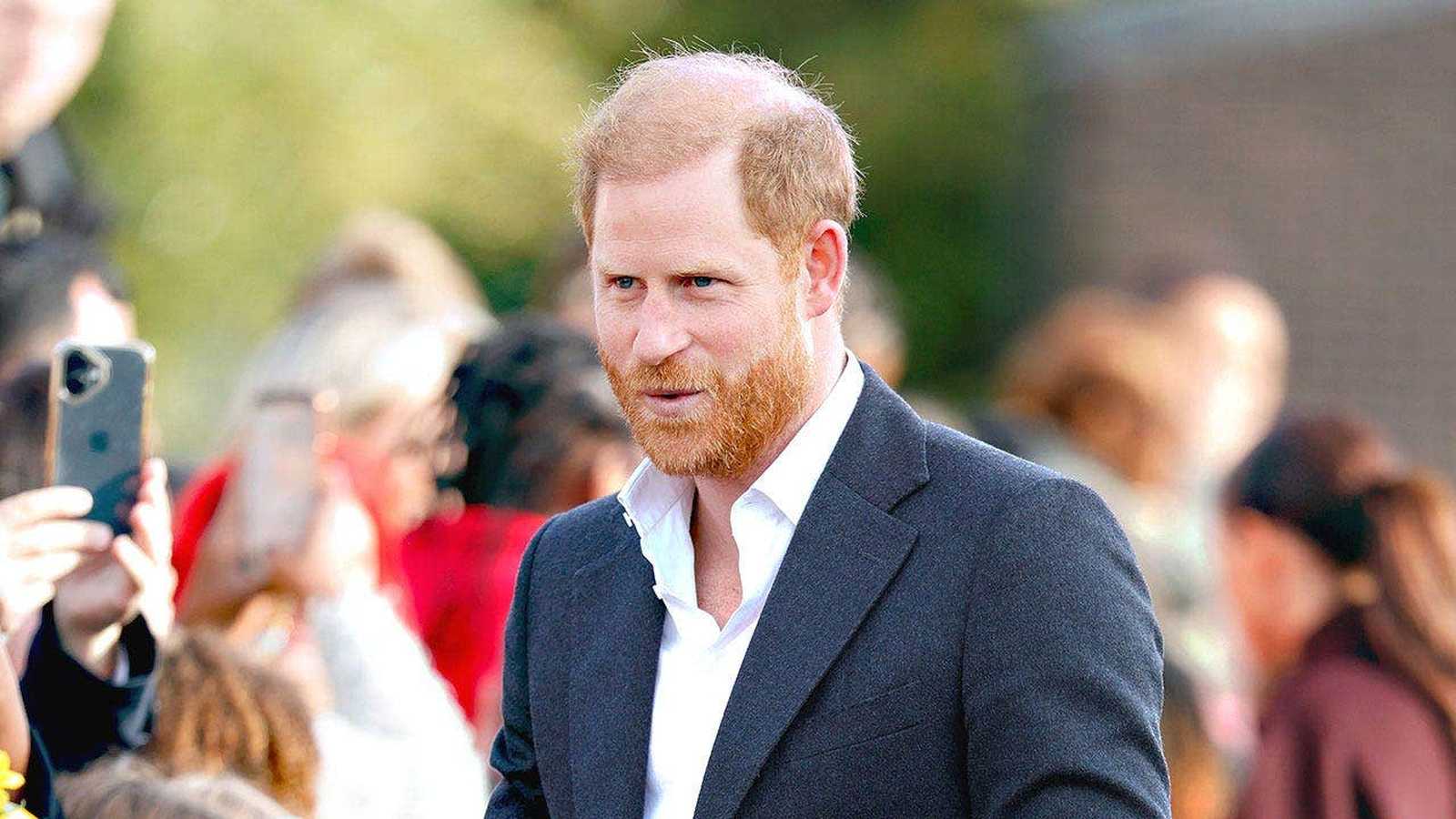 Prince Harry wearing a dark jacket and white shirt among a crowd