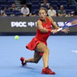 Qinwen Zheng playing tennis on a blue indoor court during a match in Beijing