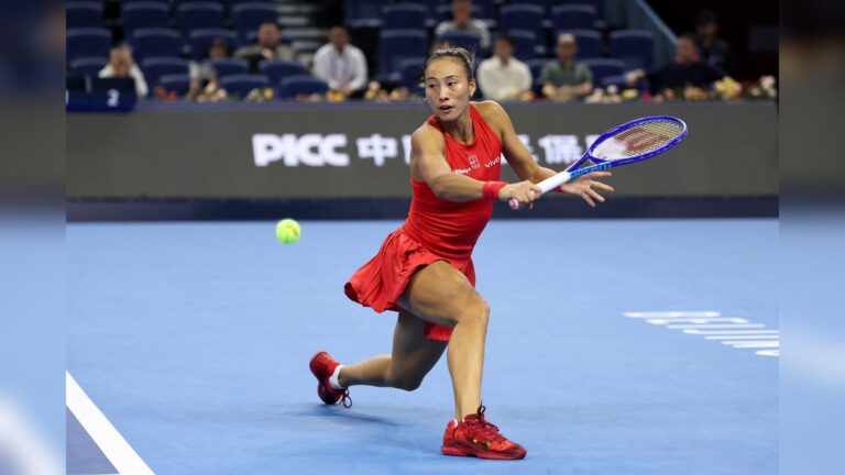 Qinwen Zheng playing tennis on a blue indoor court during a match in Beijing