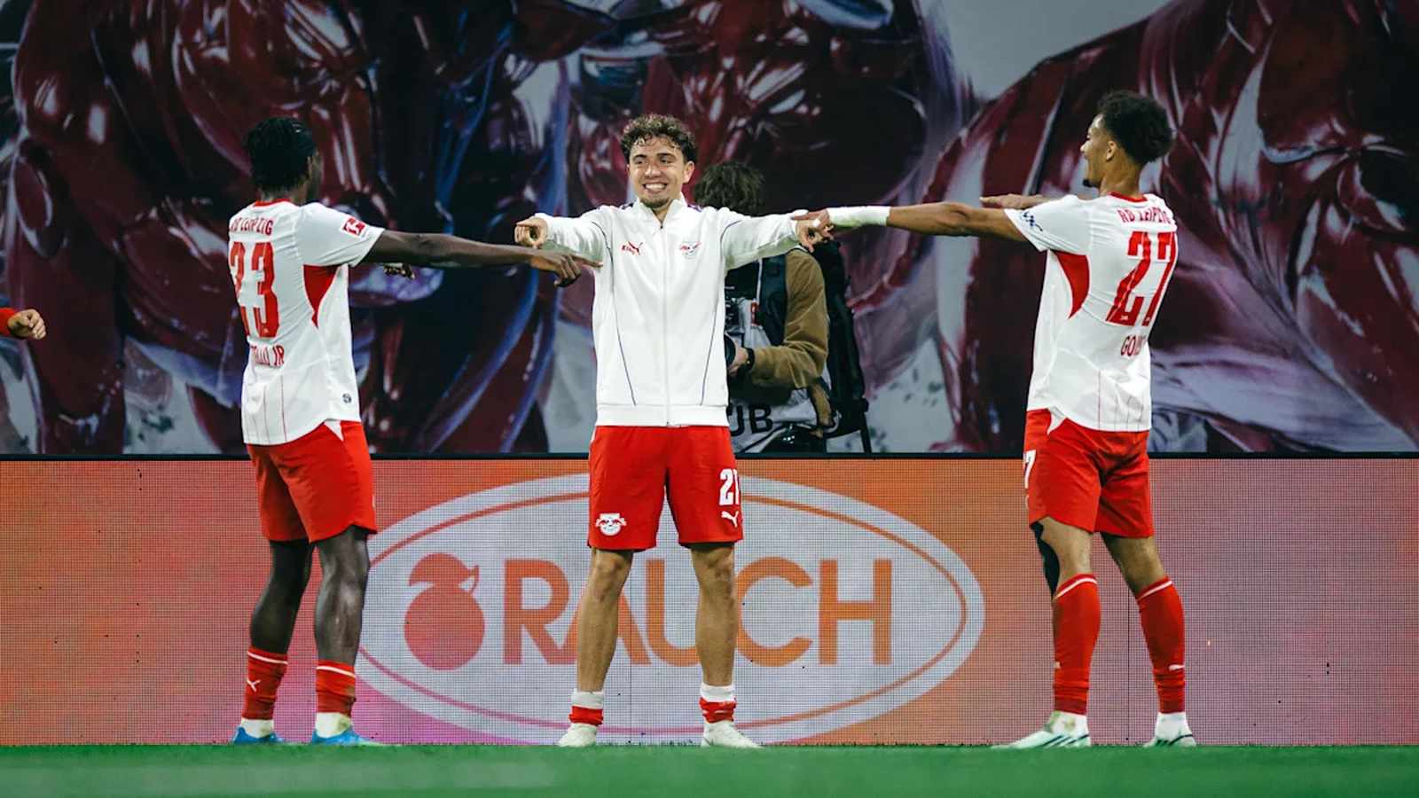 Three RB Leipzig soccer players in white and red uniforms celebrating on the field