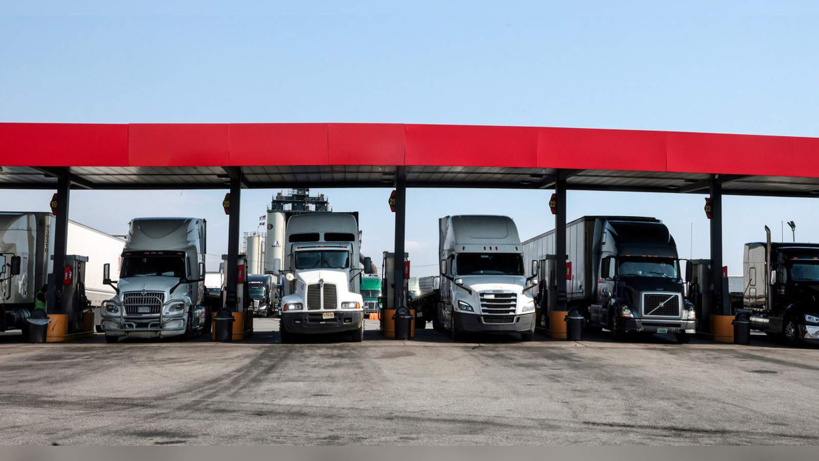 Several semi-trucks parked under a fuel station canopy waiting to refuel