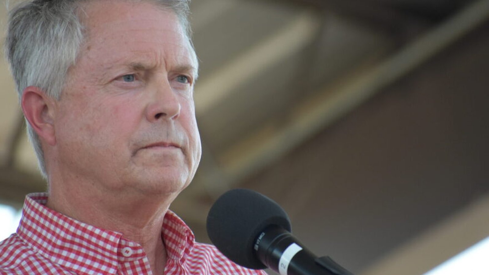 Senator Roger Marshall speaking into a microphone outdoors wearing a red checkered shirt
