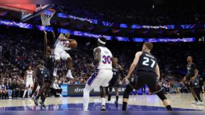 Philadelphia 76ers player drives toward the basket defended by Detroit Pistons players during an NBA