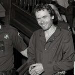 Serial killer Ted Bundy smiling while being escorted by law enforcement officers in a courthouse