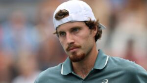 Close-up portrait of tennis player Toby Samuel wearing a white cap and teal polo shirt