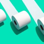 Three white toilet paper rolls unrolling across a vibrant green background