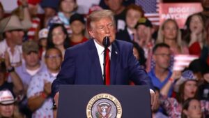 Donald Trump speaking behind a podium with presidential seal at a rally