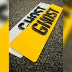 Close up of yellow and white UK ghost car number plates with raised black lettering on carpet backgr