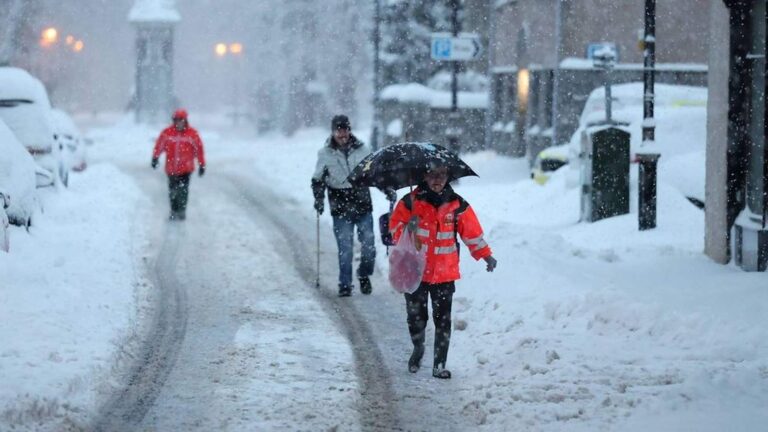 People walking along a snow-covered UK street during a heavy winter blizzard