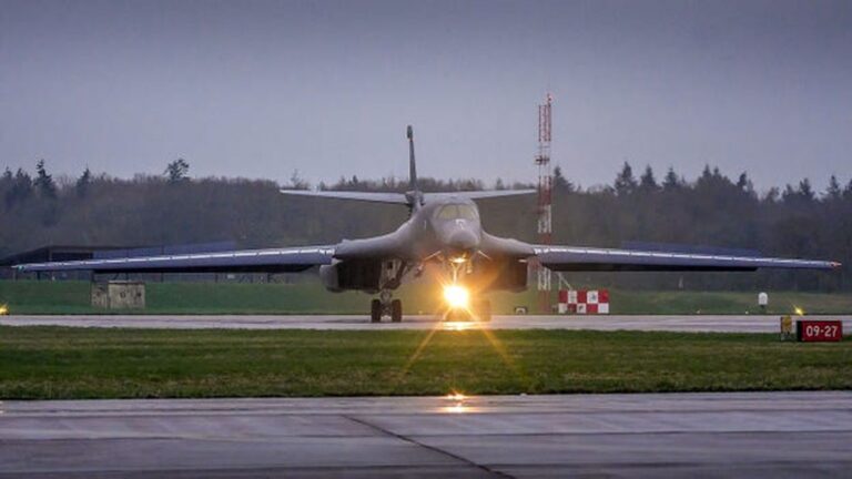 A US B-1 heavy bomber aircraft on the runway at an airbase with landing lights on