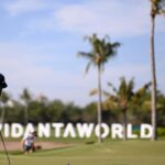 A golfer in a purple shirt putting on the green with VidantaWorld sign in the background