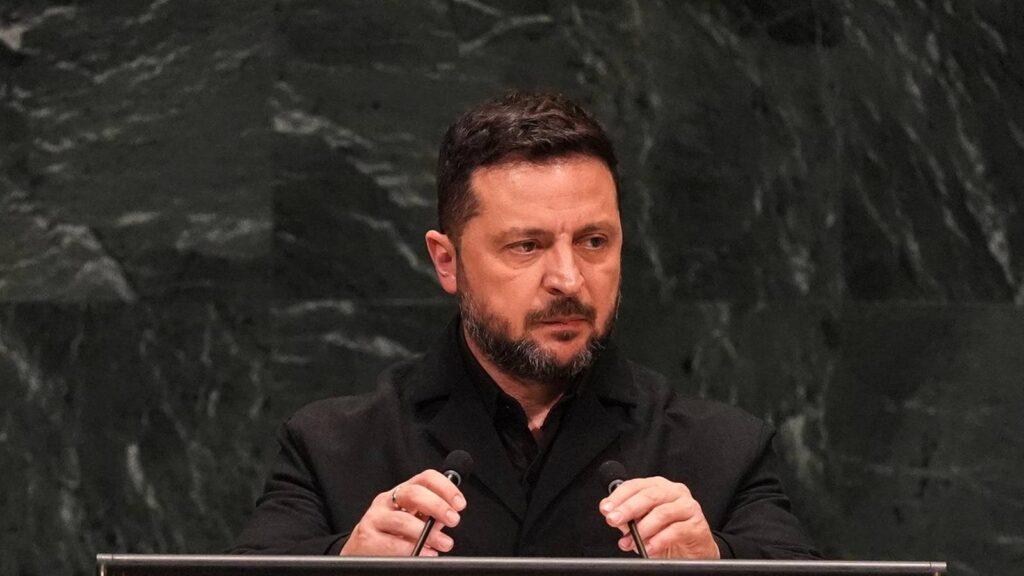 Ukrainian President Volodymyr Zelenskyy speaking behind a podium against a dark textured background