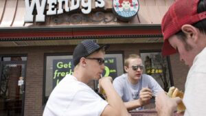 Young customers eating food at an outdoor table in front of a Wendys restaurant