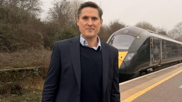 A man in a suit standing on a railway platform next to a train