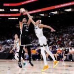 WNBA basketball players competing on the court during a game with spectators in the background