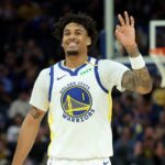 Basketball player Yaxel Lendeborg smiling and raising his hand in a Golden State Warriors uniform on