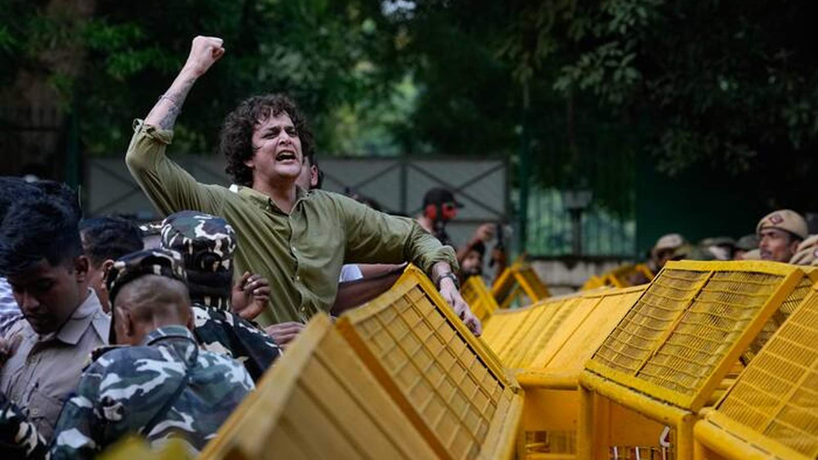 A young Indian man with a raised fist protesting behind yellow police barricades